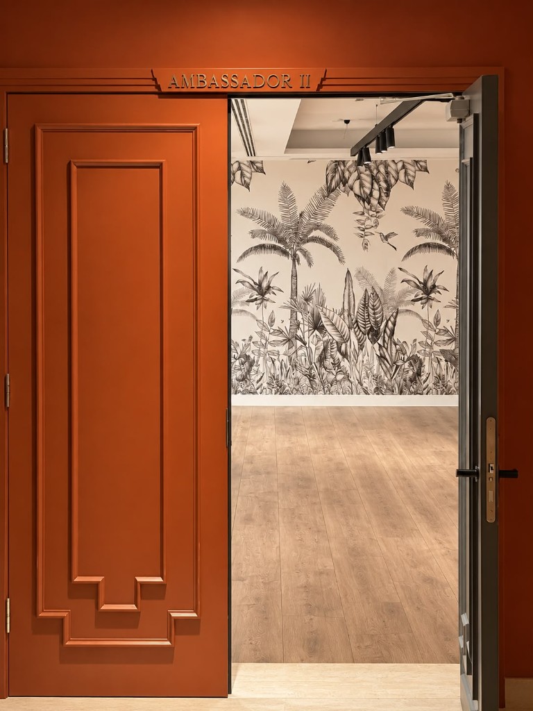 Entrada al salón Ambassador II: puerta terracota abierta hacia un interior con mural tropical en blanco y negro.
